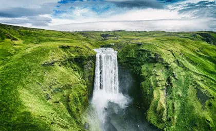 Aerial view of Skógafoss Waterfall surrounded by lush green hills, showcasing the natural beauty of Iceland's South Coast on a seven day guided tour around Iceland.