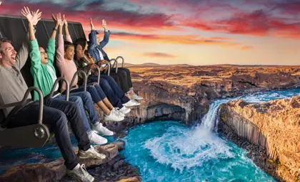 Group of visitors enjoying FlyOver Iceland's immersive experience, suspended over a scenic Icelandic waterfall landscape, with vibrant sunset skies in the background.