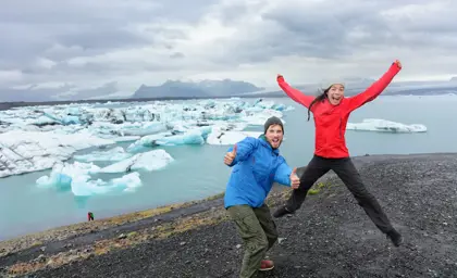 Excited couple jumps with joy by Jokulsarlon glacier lagoon in Iceland during an adventure tour.