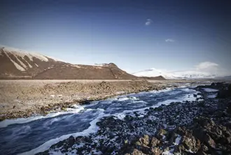 Snowy landscape view of Langjökull glacier with river stream in foreground.