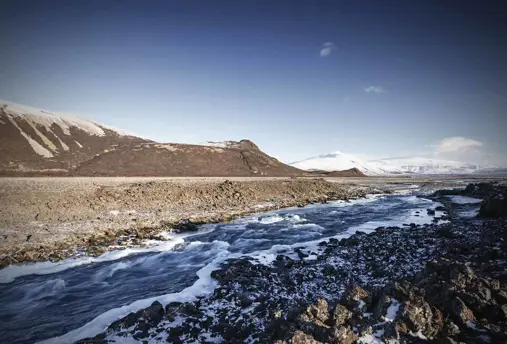 Snowy landscape view of Langjökull glacier with river stream in foreground.