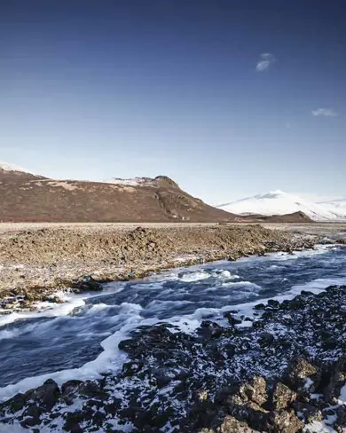 Snowy landscape view of Langjökull glacier with river stream in foreground.