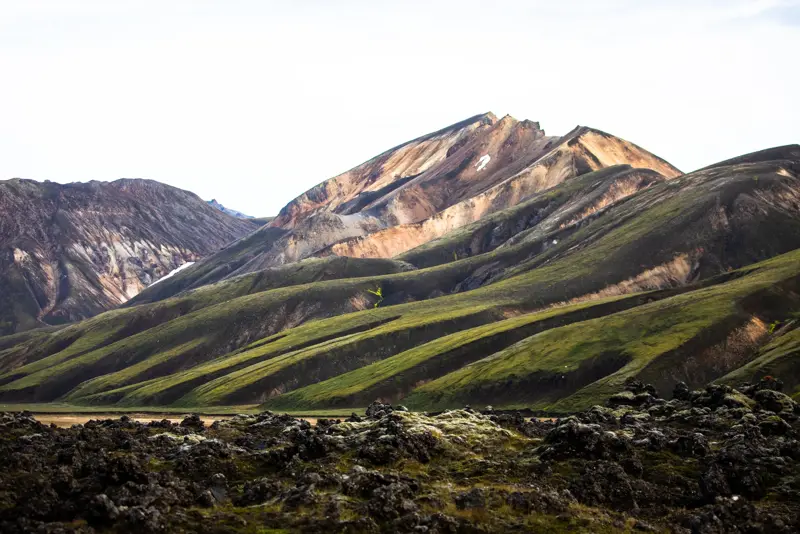 The iconic colorful rhyolite mountains of Landmannalaugar with green moss and lava fields in the foreground.