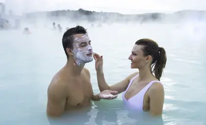Couple enjoying the Blue Lagoon geothermal spa in Iceland as the woman applies a white silica clay mask to the man's face during a romantic wellness retreat.