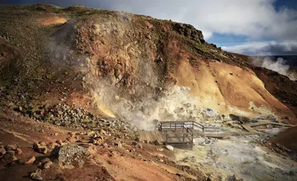 Steam rising from the geothermal area of Krýsuvík, Iceland, with rugged orange hills and wooden walkways.