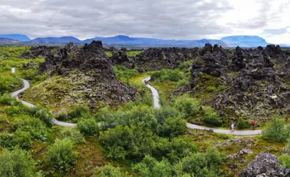 Dimmuborgir lava rock formations surrounded by lush green vegetation in Mývatn, Iceland, with a walking trail weaving through the landscape.