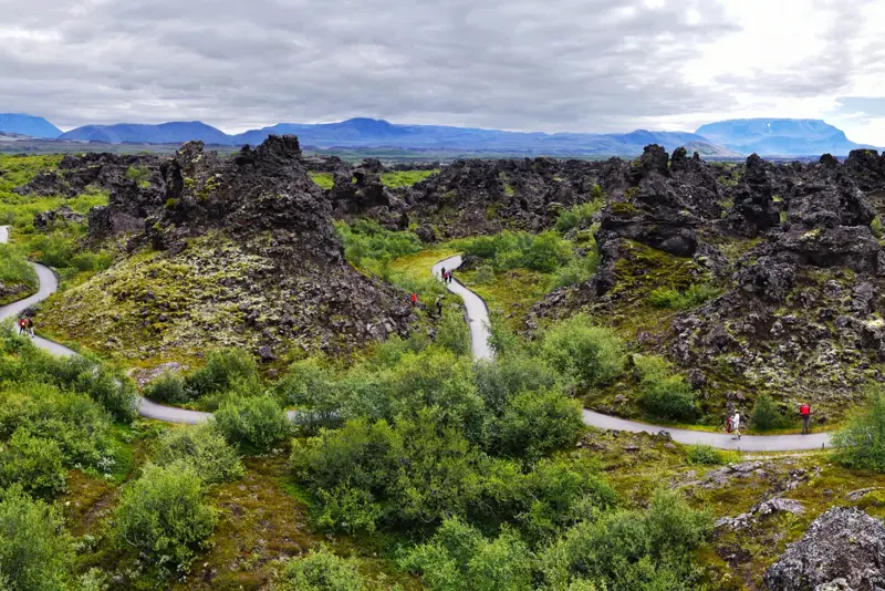 Dimmuborgir lava rock formations surrounded by lush green vegetation in Mývatn, Iceland, with a walking trail weaving through the landscape.