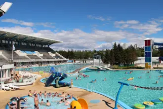 Families and visitors enjoying the various pools, slides, and hot tubs at Laugardalslaug swimming complex in Reykjavik, Iceland, on a sunny day.