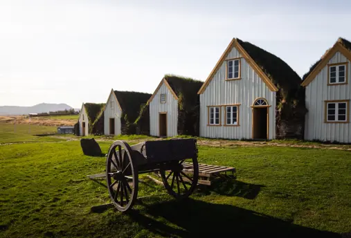 Glaumbær turf house museum and farm with old fashion cart outside and blue skies above.
