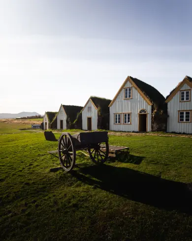Glaumbær turf house museum and farm with old fashion cart outside and blue skies above.