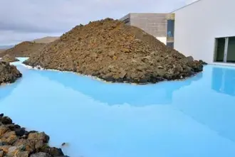 Exterior of the Blue Lagoon building with waters reaching the walls and lava rocks around.