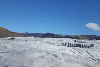 Group of hikers exploring Sólheimajökull Glacier under a bright blue sky, with expansive ice fields and distant mountains, capturing the adventure of glacier hiking in Iceland.