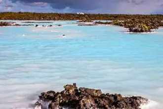 The milky waters of the Blue Lagoon with lava rock sticking out of the waters and a private shuttle in the distance. 