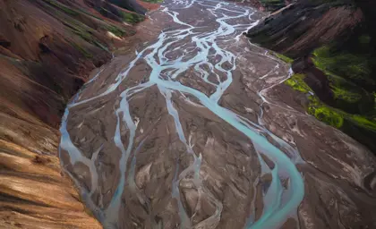 An aerial view of a braided river in Landmannalaugar winding through a valley, surrounded by mountains.