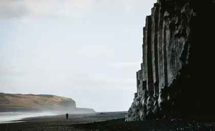 Basalt columns at Reynisfjara Black Sand Beach in Iceland with a lone figure walking along the shore, famous for its dramatic rock formations and volcanic landscape.
