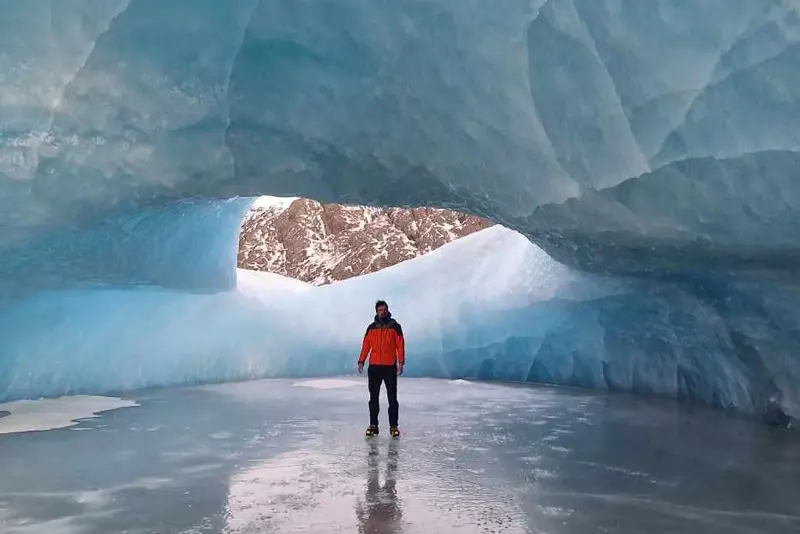 A person standing inside a stunning blue ice cave during a South Shore Blue Ice Cave Tour with Travel Reykjavík.