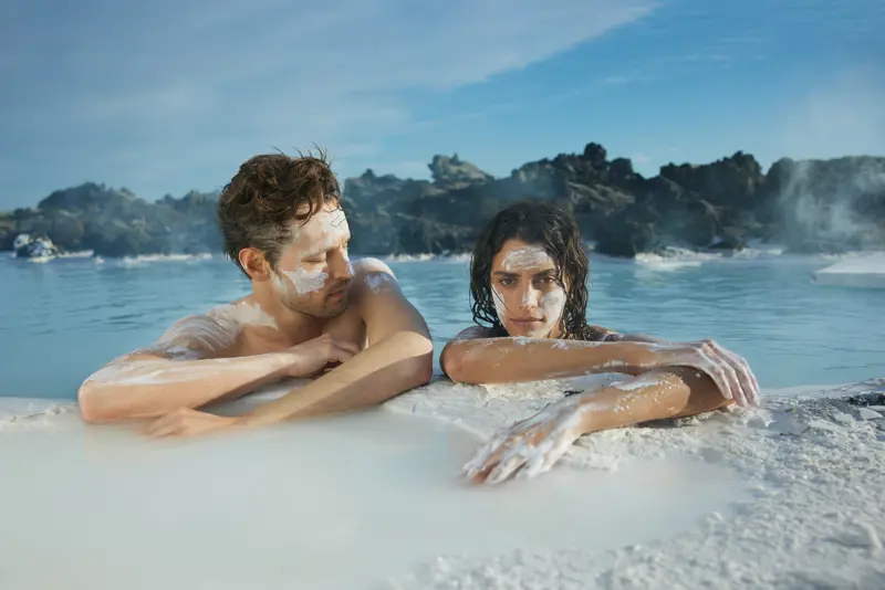 Couple enjoying geothermal spa experience at Blue Lagoon Iceland, applying natural silica face masks for skin rejuvenation.