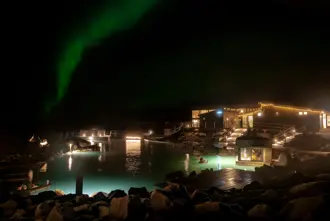 Mývatn Natur Baths Geothermal Spa at night with Northern Lights in the sky above with the spa buildings warmly lit.