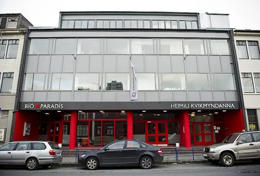 Front view of Bió Paradís cinema in Reykjavík, Iceland, showcasing its modern architecture with red accents and parked cars outside.
