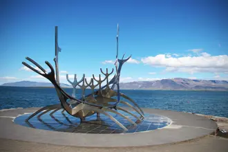 The Sólfarið Sun Voyager sculpture in Reykjavik, Iceland, set against a backdrop of blue skies and distant mountains.