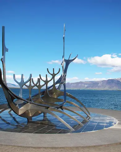 The Sólfarið Sun Voyager sculpture in Reykjavik, Iceland, set against a backdrop of blue skies and distant mountains.