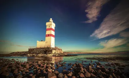 The Reykjanesviti lighthouse standing tall against a clear sky, surrounded by rocky terrain in Iceland.