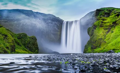 Skógafoss Waterfall in Iceland surrounded by lush green cliffs, a must-see stop on Travel Reykjavik's stopover day tours.