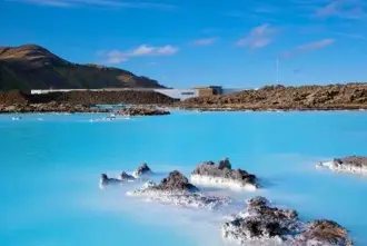 Blue Lagoon in Iceland with rocky lava standing up from the blue waters under a blue sky.