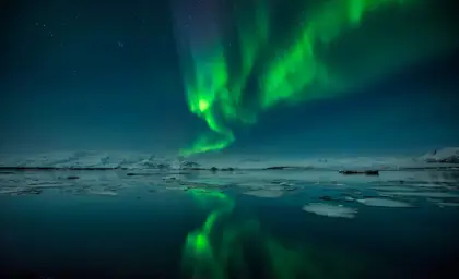 Northern Lights reflecting on the waters of Jökulsárlón Glacier Lagoon during a winter night on 3 day northern lights tour around Iceland.