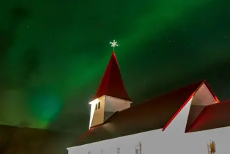 Vikurkirkja Church under green Northern Lights over Vik in Myrdal.