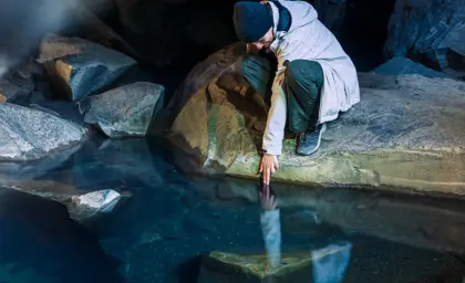 Man touching crystal-clear water inside Grjótagjá cave in Iceland, surrounded by volcanic rock formations