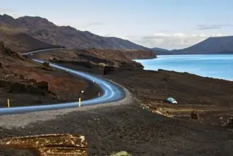 Road on Reykjanes peninsula between Keflavik airport and Reykjavik with a car stopped next to a lake.