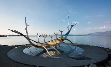 Sun Voyager sculpture (Sólfarið) by the sea in Reykjavik, Iceland, with clear blue skies and distant mountains in the background.