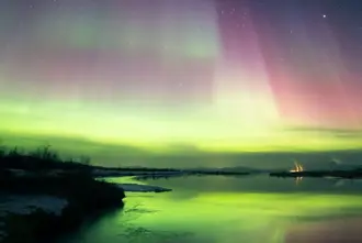 Iceland's Thingvellir on Golden Circle route under Northern Lights in green and pink colors over frozen lake.
