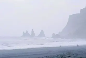 Black Sand Beach with people walking on it in the fog close to Vik I Myrdal.